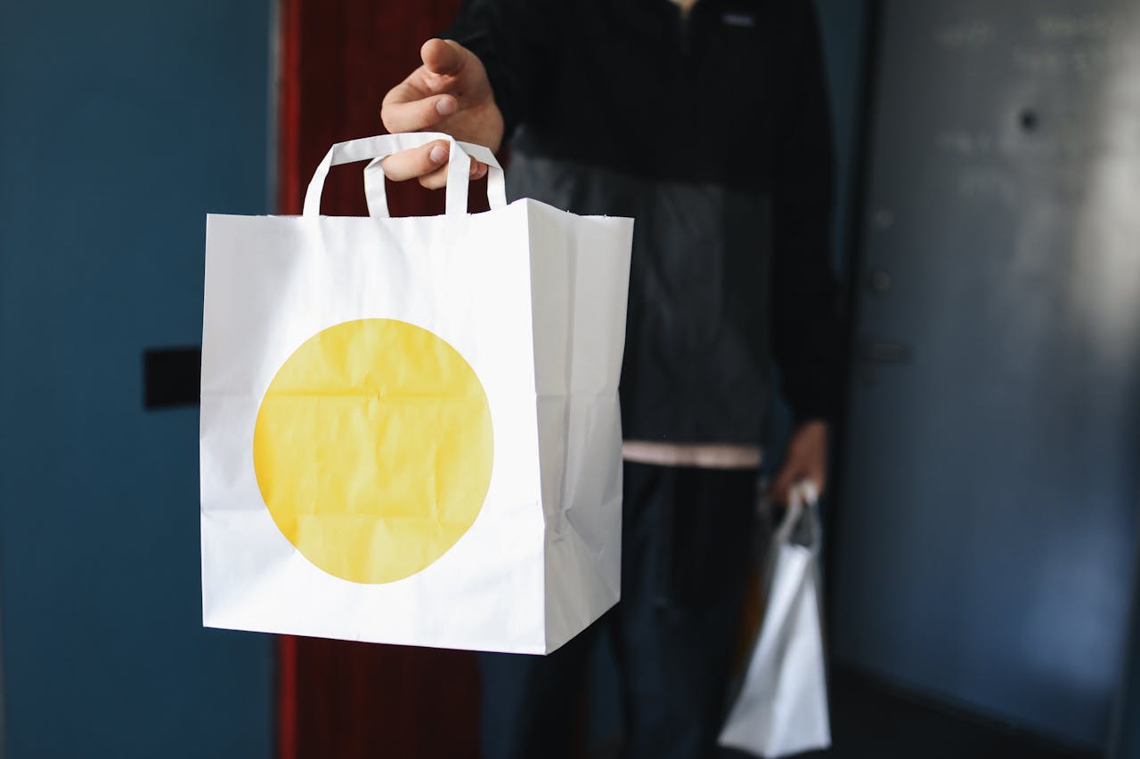 Close-up of a person holding a white paper bag with a yellow circle design, suggesting delivery or shopping.