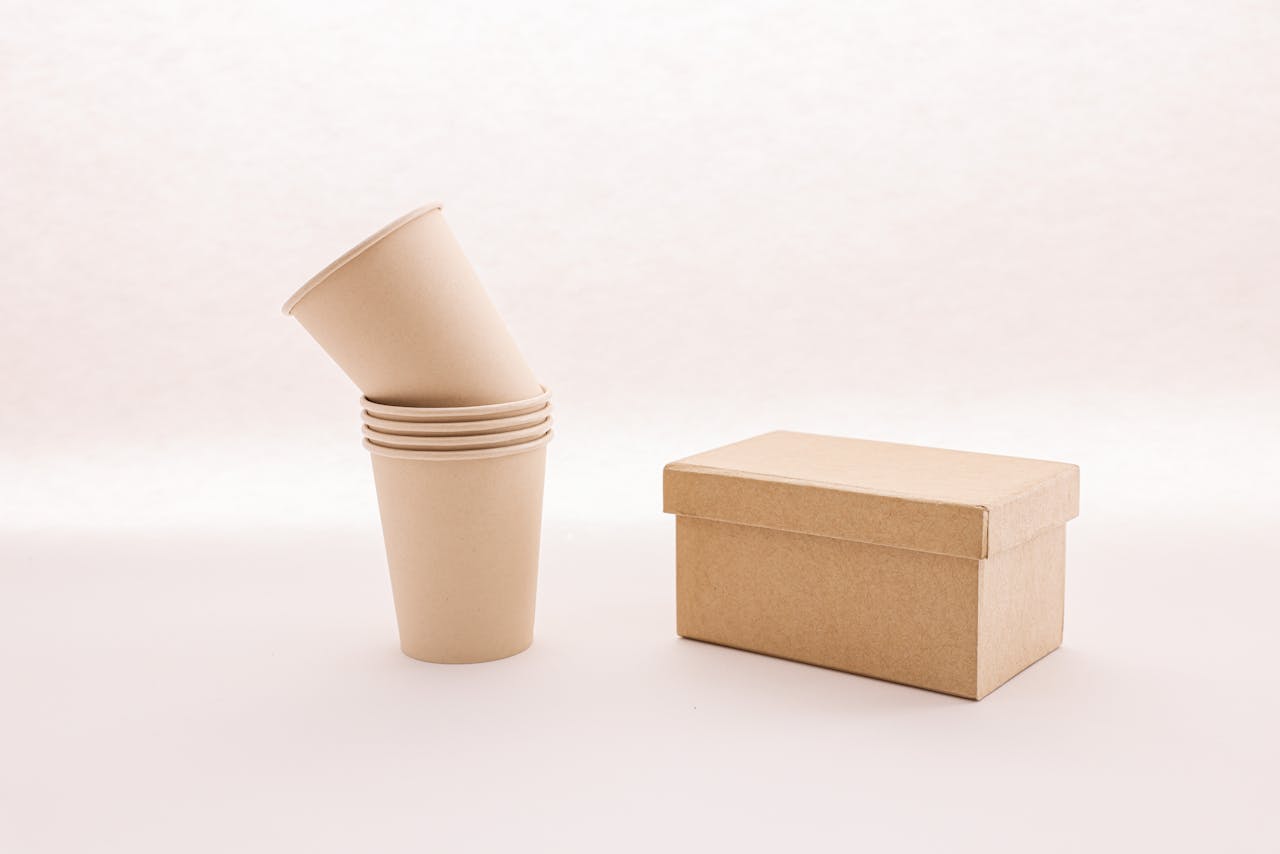 A stack of eco-friendly cardboard cups next to a closed box on a white background.